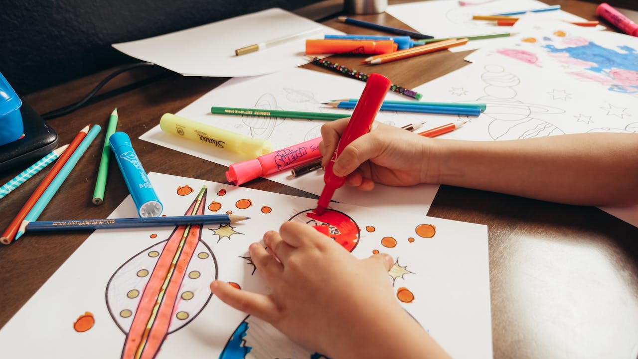 why-choose-us A child coloring a space-themed picture with colored pencils and markers on a desk.