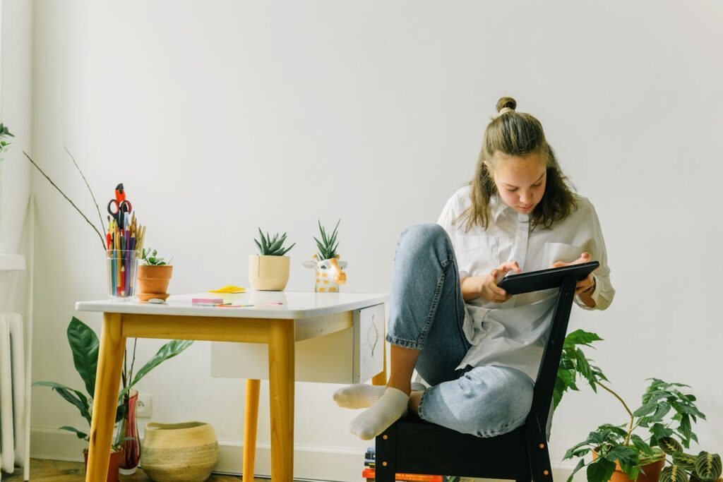pexels photo 7695252 A teenage girl using a tablet while sitting in a modern home workspace with plants.