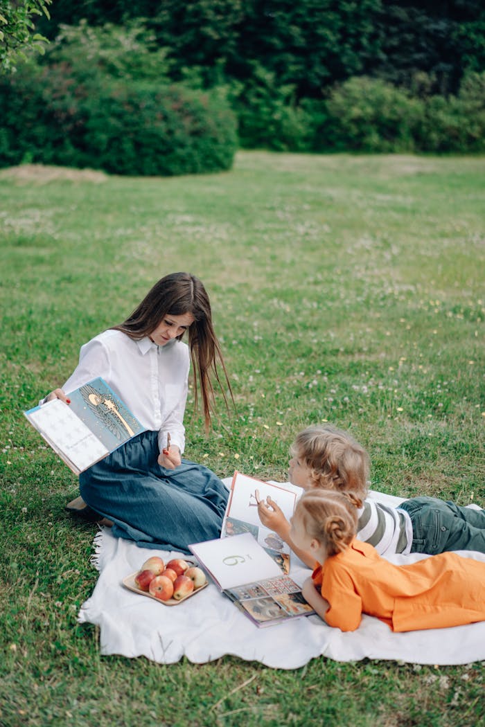 gallery-2 A woman reads to children on a picnic blanket with apples in a scenic garden.
